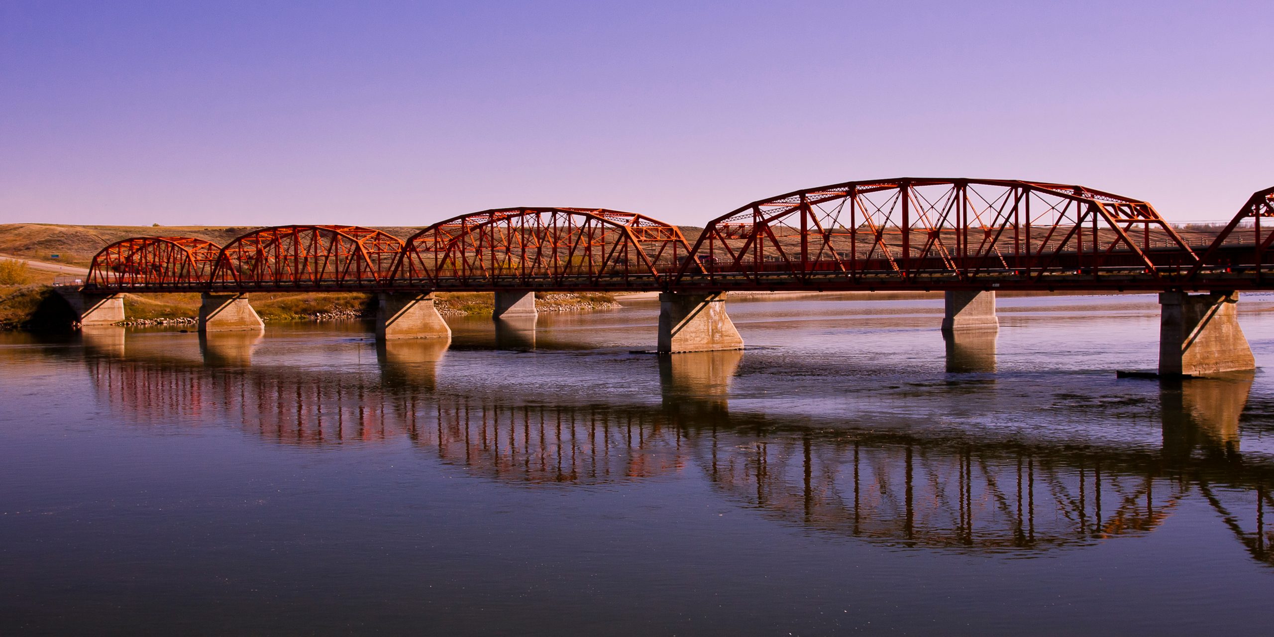 Old red bridge over the calm waters of the Saskatchewan River near Outlook on the Canadian Prairies.